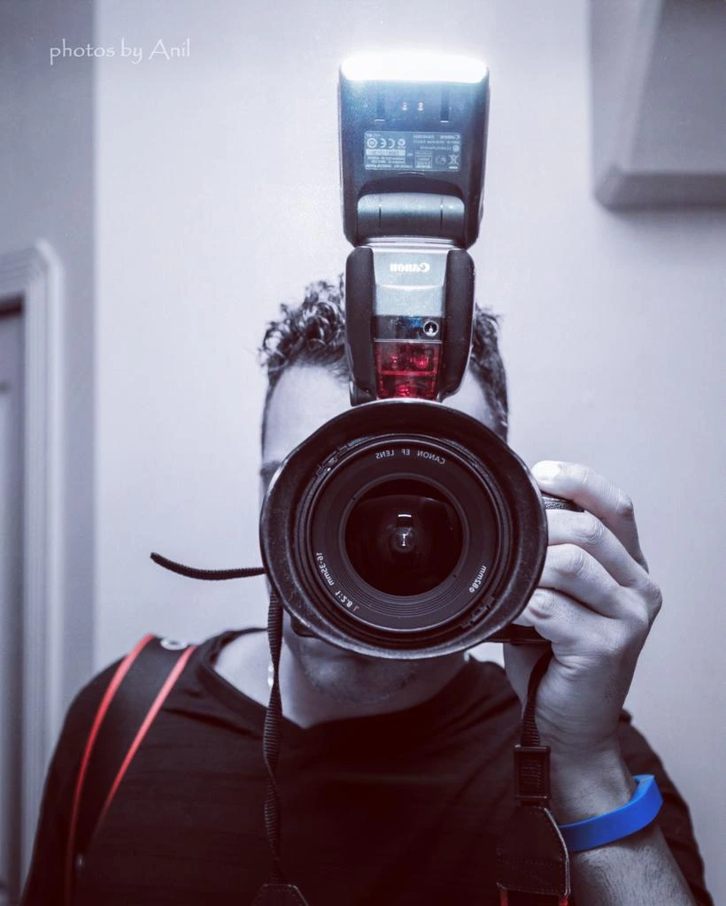 A digital SLR body with a speedlight mounted, held up in both hands against a white wall