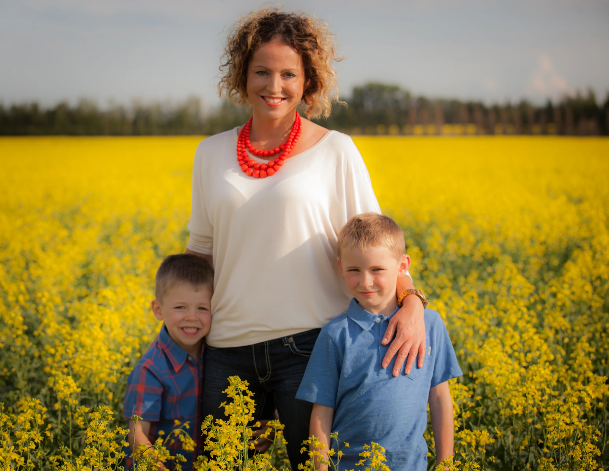 A mother standing waist-deep in blooming canola with her two young sons