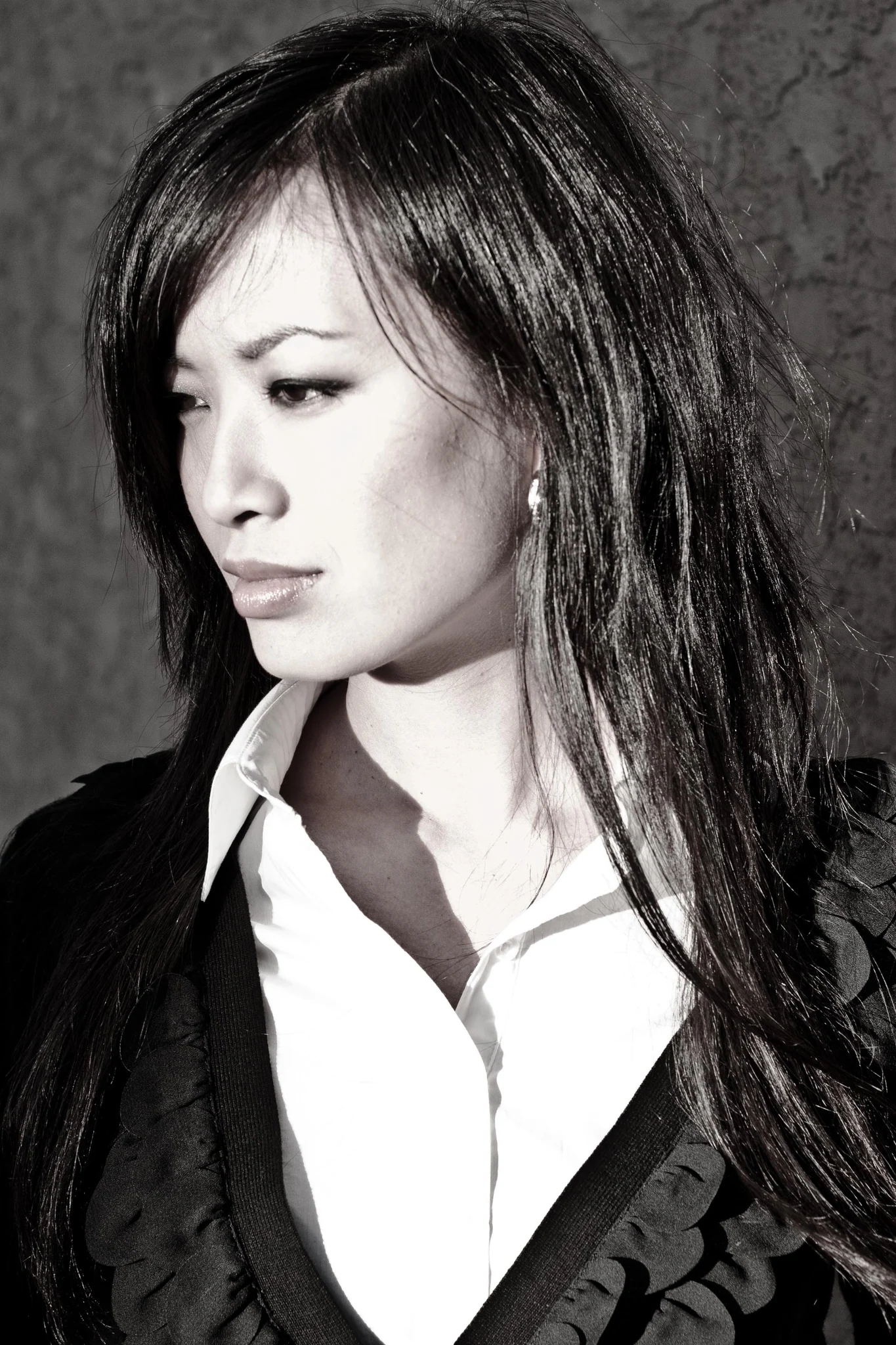 A studio portrait of a woman in a dark blouse, lit low against grey, in black and white