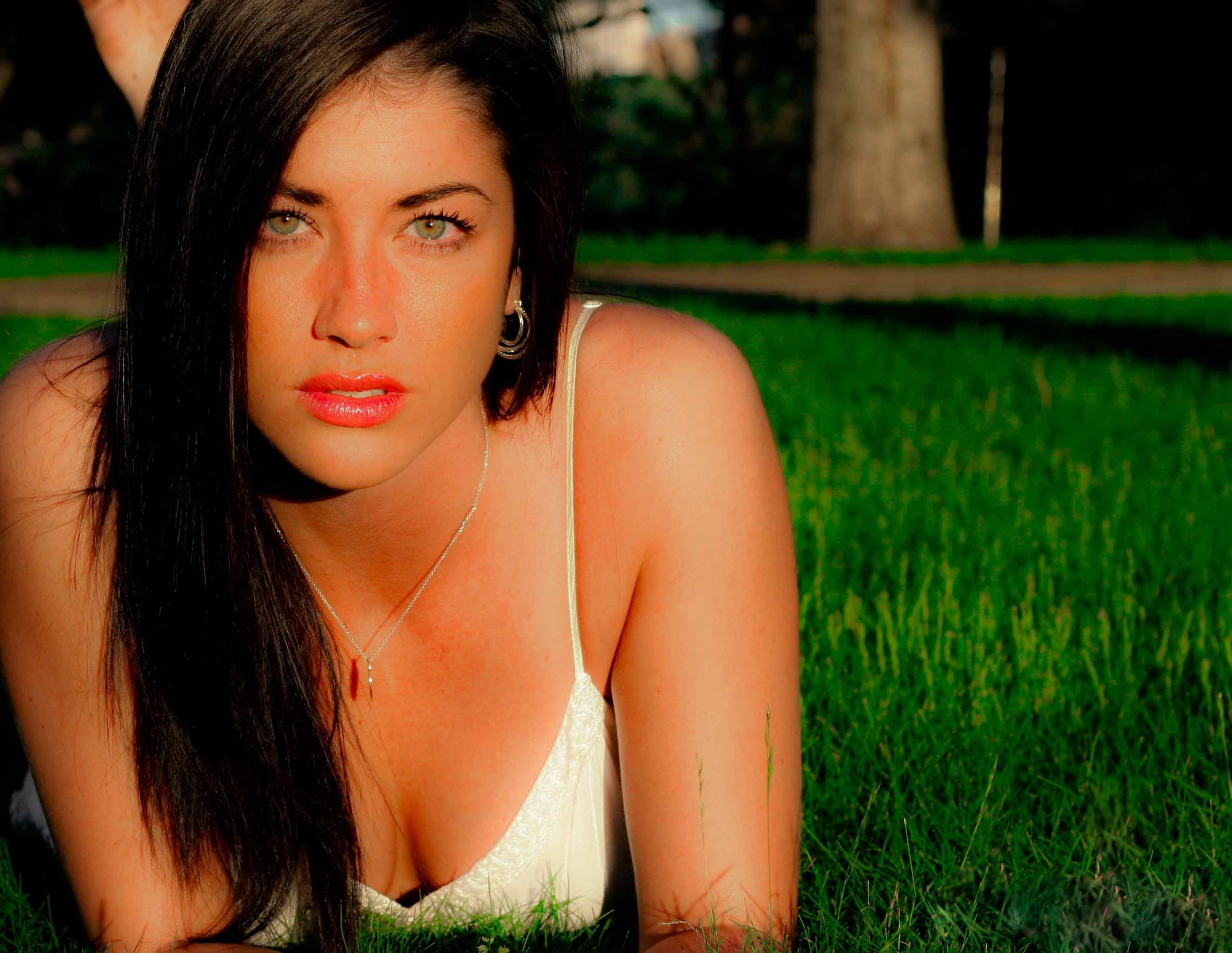 A woman lying in long grass in low evening light, looking up at the camera