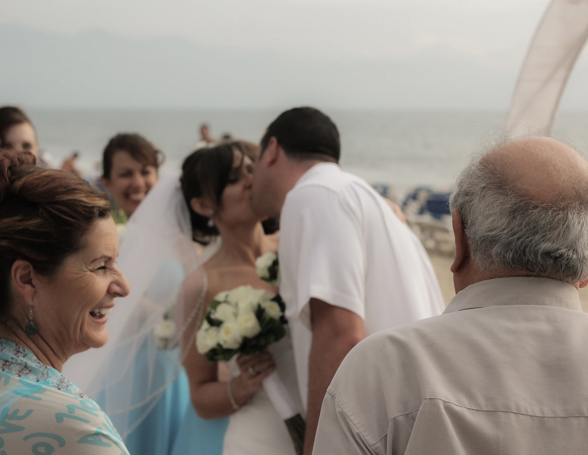 A couple kissing at a lakeside ceremony while their families look on