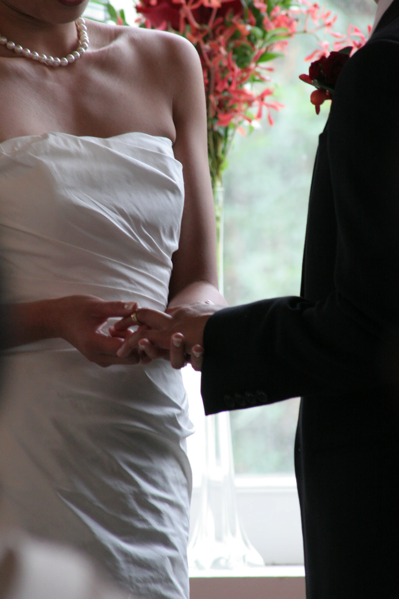 Hands meeting during the ring exchange, the bride's gown catching window light